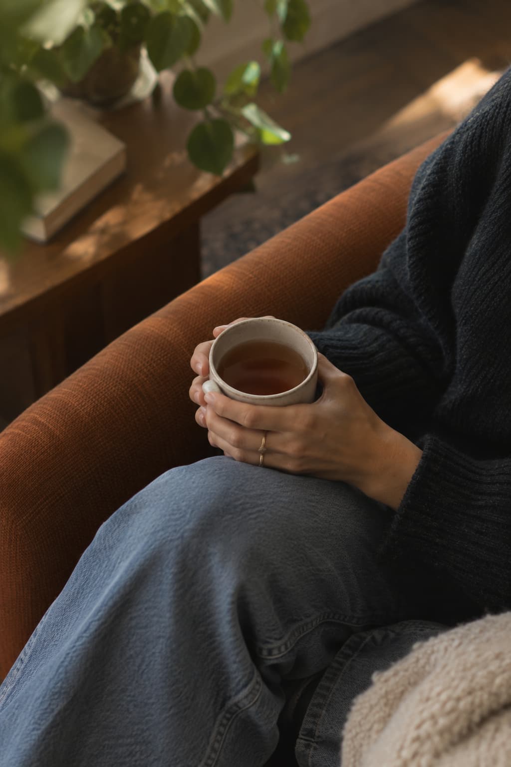 A cup of tea held in both hands beside a sunlit window