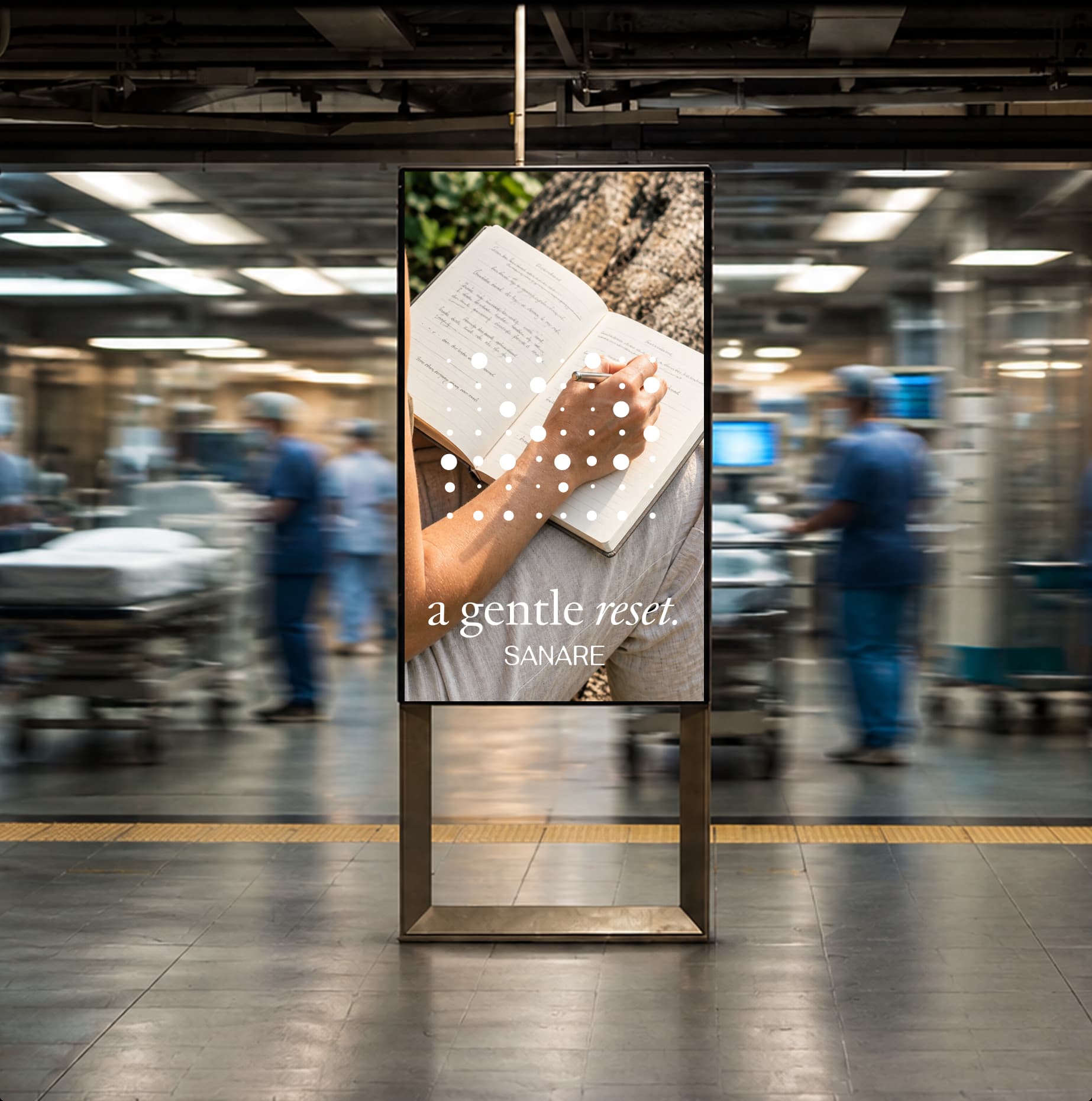 A calm 'a gentle reset' Sanare sign, a hand writing in a journal, set against a blurred, busy hospital corridor